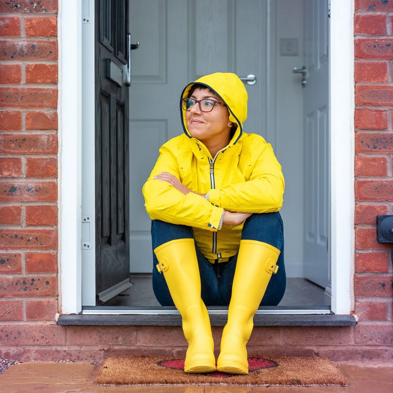 Frau mit Gummistiefeln und Regenjacke sitzt vor der Tür