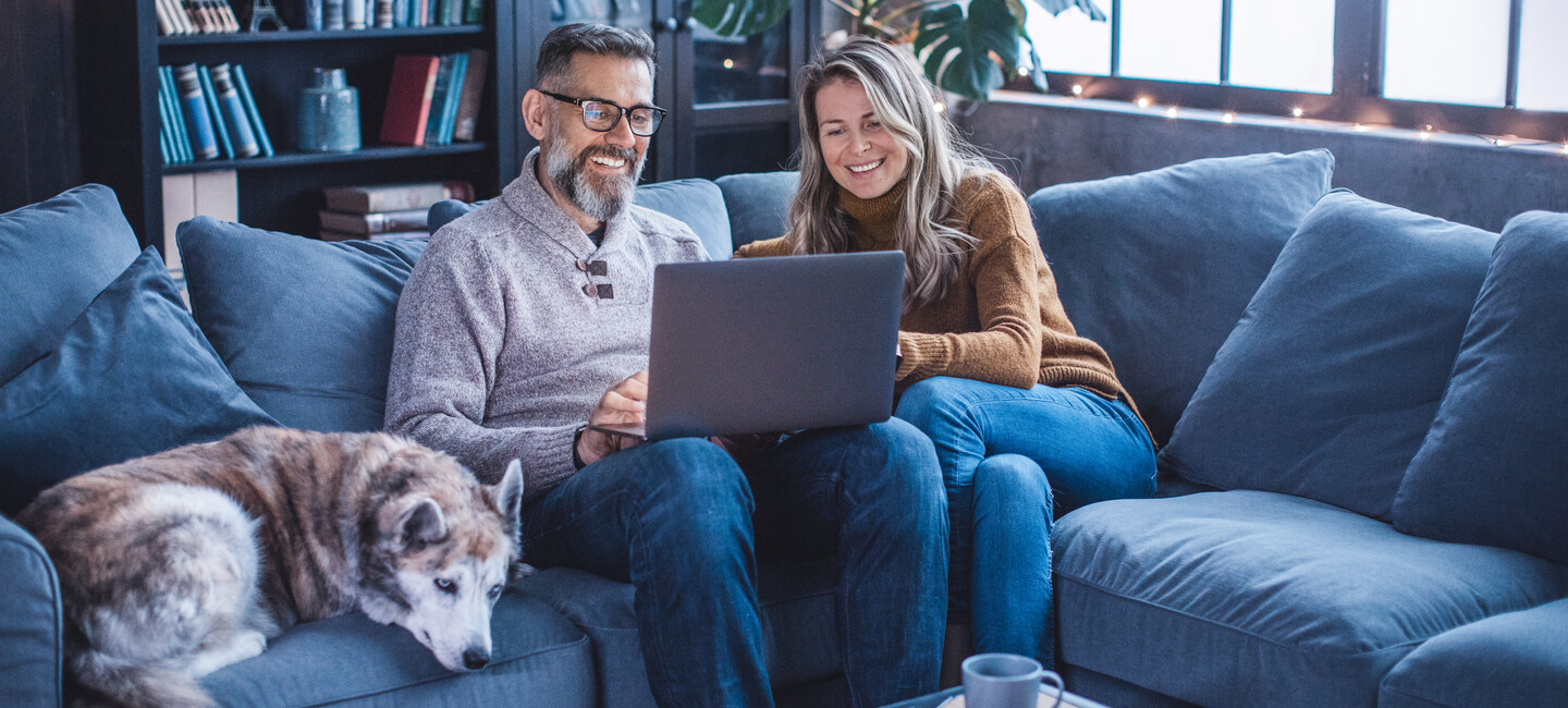 Frau und Mann sitzen auf einem Sofa und schauen auf einen Laptop