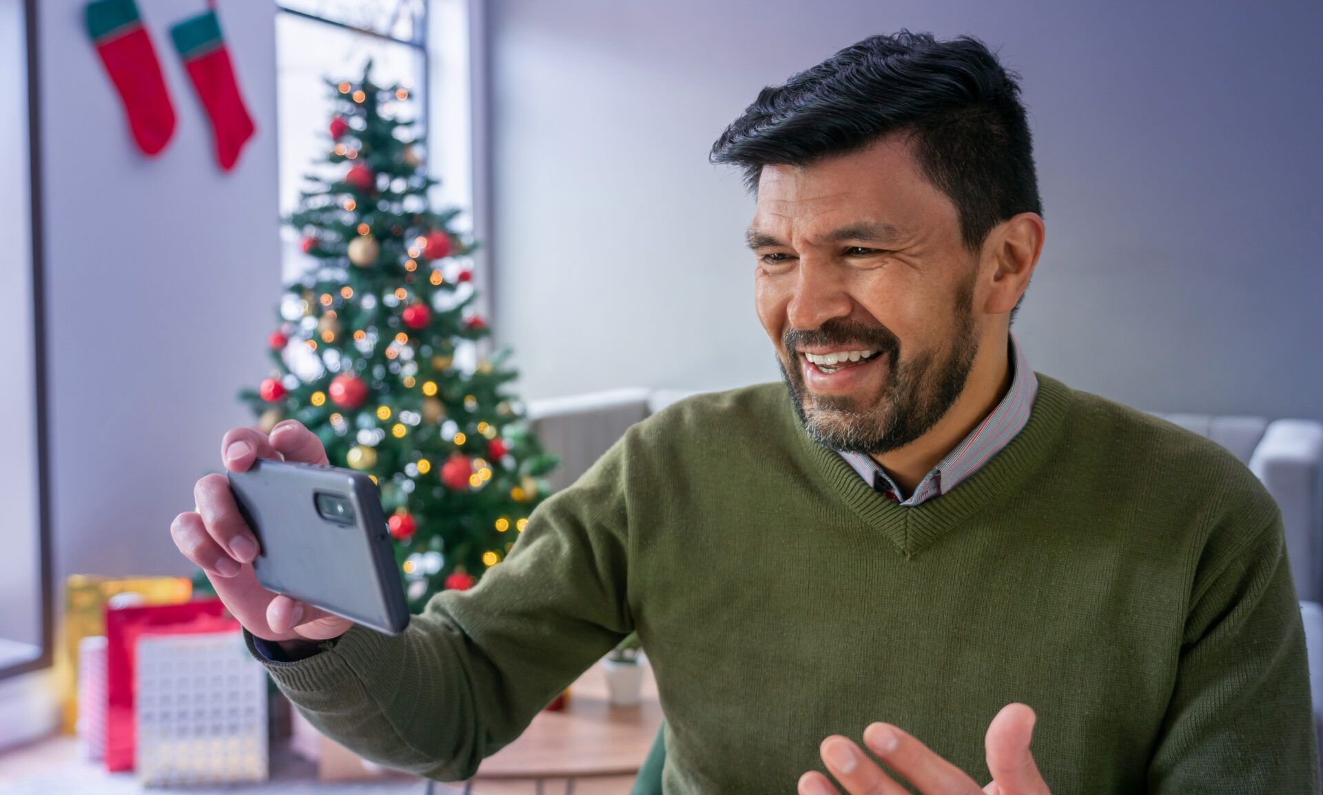 Mann mit Handy macht Video von sich vor Weihnachtsbaum