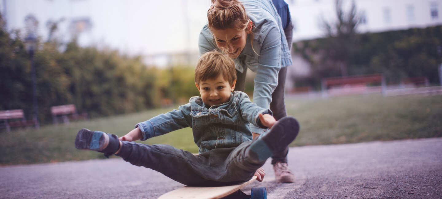 Kleiner lachender Junge und seine Mutter haben Spaß am Skateboardfahren