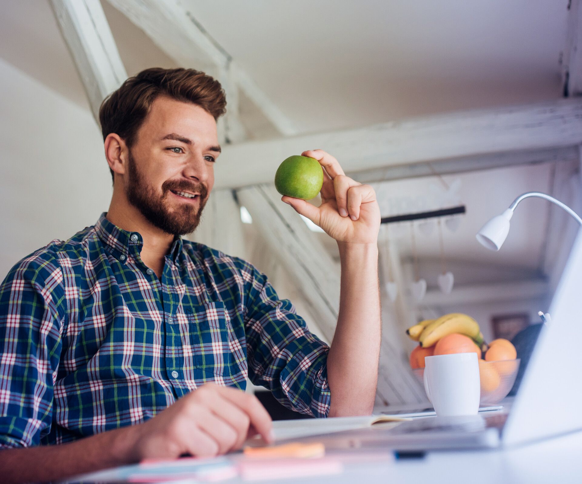 Mann am Laptop mit Apfel in Hand