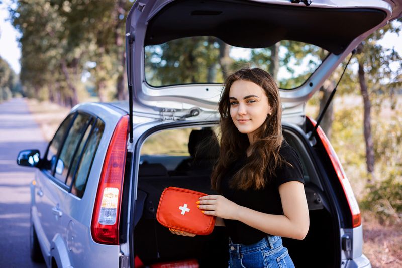 Frau mit Erste-Hilfe-Kasten am Auto