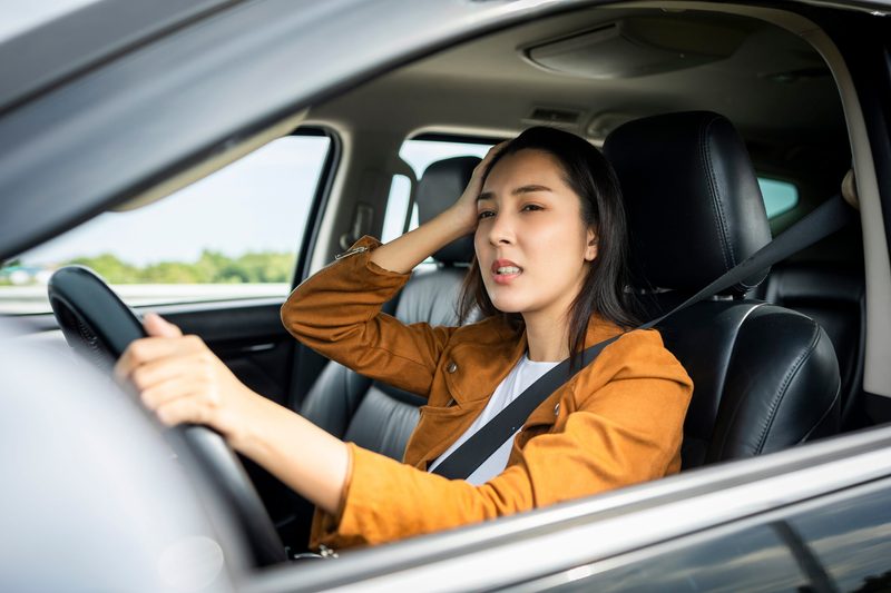 Frau greift sich an den Kopf im Auto
