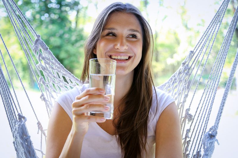 Frau trinkt Wasser in Hängematte