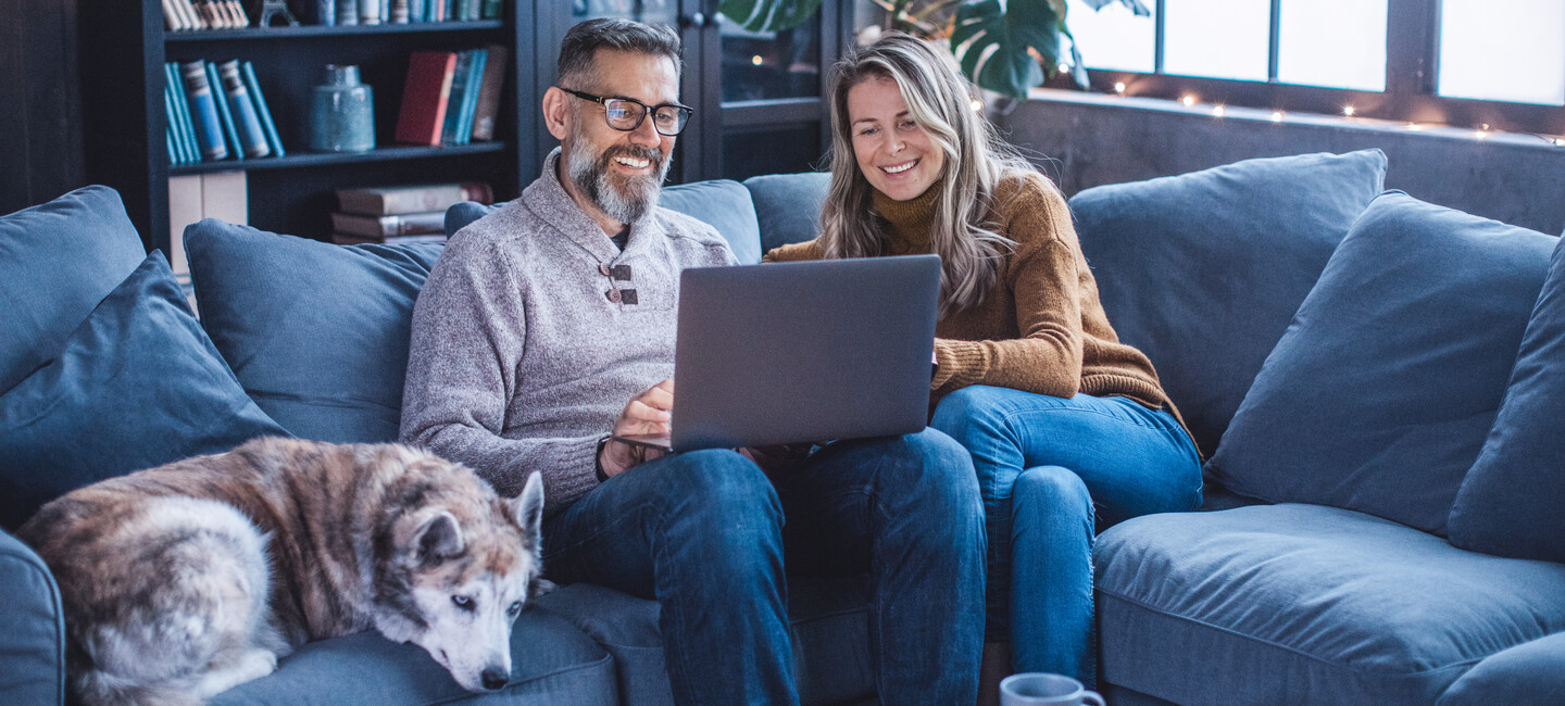 Reifes Paar sitzt auf der Couch vor dem Notebook