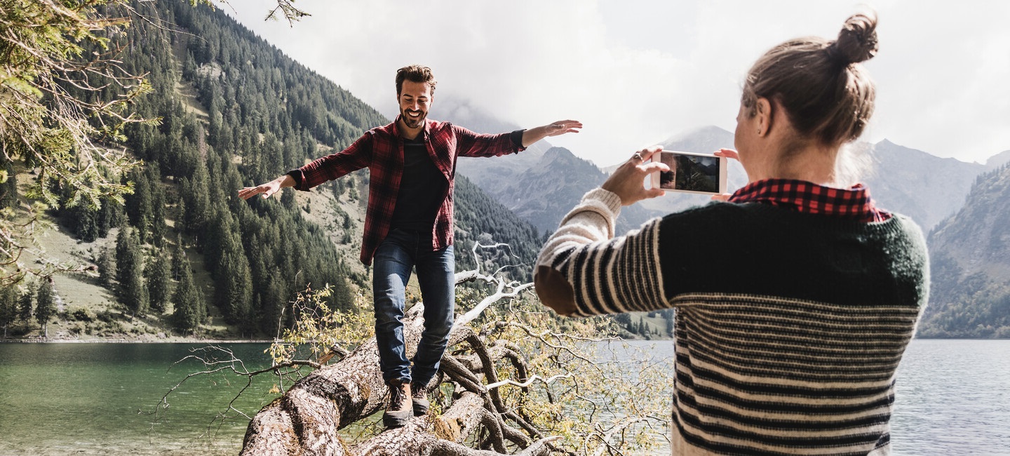 Mann-balanciert-auf-baumstamm-frau-fotografiert